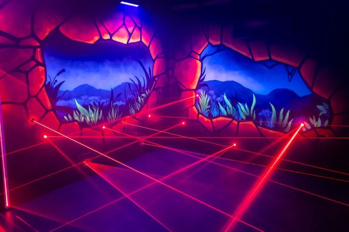 Roter Laserstrahlen-Parcours in einem dunklen Raum mit leuchtenden Felswänden.